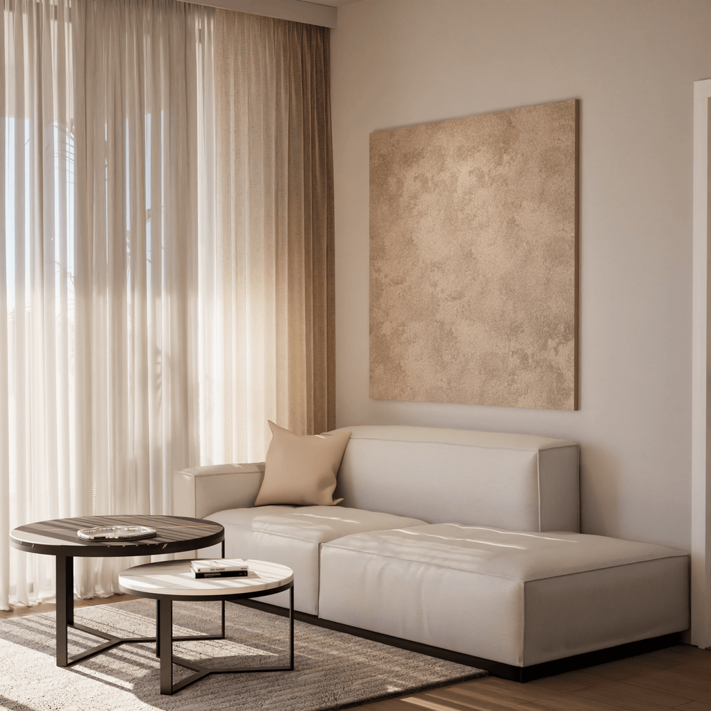 Minimalist living room with a modern beige sofa, nested coffee tables, textured wall art, and soft natural light through sheer curtains